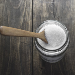 Sugar in wooden spoon and glass jar
