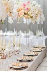 Tall bouquet of white orchids and beige roses stand on dinner table