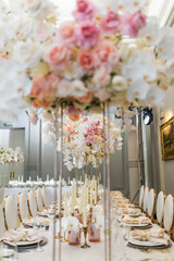 Tall square vases with elegant pink roses and orchids on dinner table