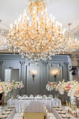 Fototapeta na wymiar Golden chandelier with shiny lamps hangs over dinner tables
