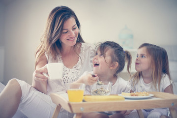 Mother with her little daughters having breakfast in the bed.