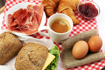 breakfast on table with bread rolls, croissants, coffe and eggs