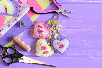 Cute hearts keyring. Homemade felt and fabric keyring or bag charm. Scissors, pliers, felt, needle, thread, scrap, fabric on wooden background with copy space. Set to create beautiful crafts. Top view