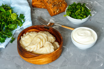 Cooked eastern european dumplings, vareniki with sour cream with parsley on gray background.