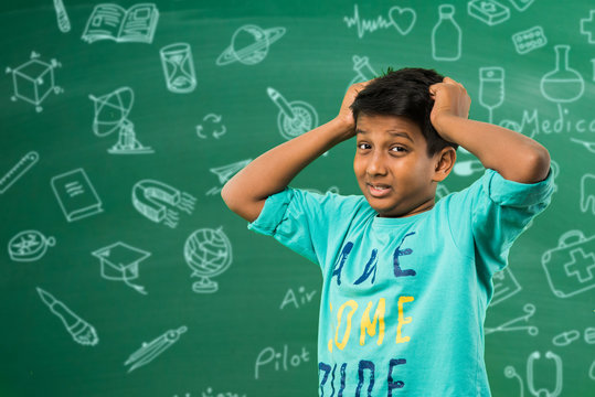 Indian School Kid Or Boy Pulling Hair In Sadness Or Distress Because Of Study Pressure Or Competition, Standing Isolated Over Green Chalkboard Background