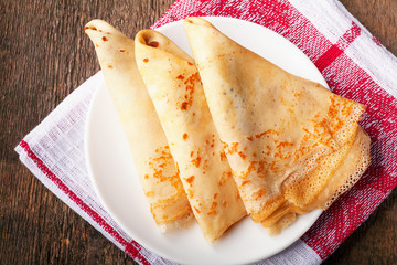 Homemade wheat crepes or pancakes with strawberry jam or marmalade stacked on a plate on a wooden...