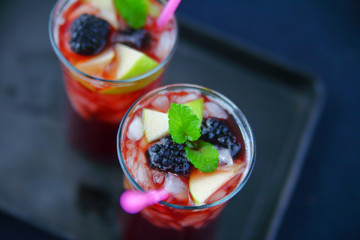 Two wine cocktails with fresh apple, blackberries and mint on ice with a dark tray