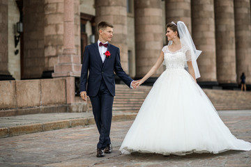 Fototapeta na wymiar Bride and groom hold each other hands tender walking around the building