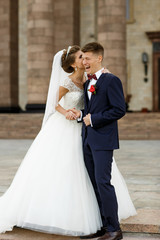 Fototapeta premium Funny wedding couple poses outside before brown building