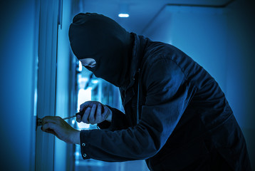 Robber with black tights over the head breaking the door lock. Black and white. Low key. Selective...