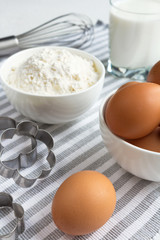 Eggs, flour and various ingredients and utensils cooking homemade cakes on the white tablecloth in blue cage concept of domestic supply Flat lay