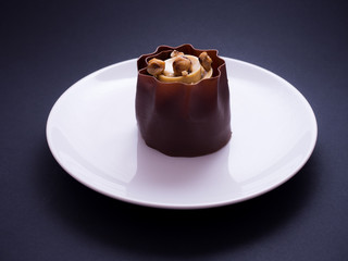 French caked named success praline with roasted hazelnuts, praline cream and chocolate, placed on white plate and isolated on dark background