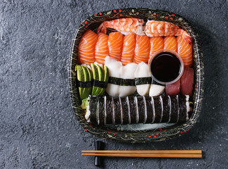 Sushi Set nigiri and sushi rolls in plastic food delivery box with soy sauce and chopsticks over black stone texture background. Top view with space. Japan menu