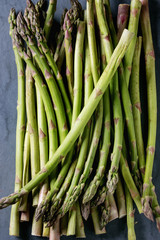 Bundle of young raw uncooked organic green asparagus over gray blue metal texture background. Top view. Healthy eating