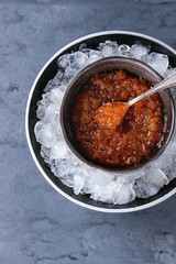 Bowl of red caviar on ice with spoon served over gray blue texture background. Top view with space