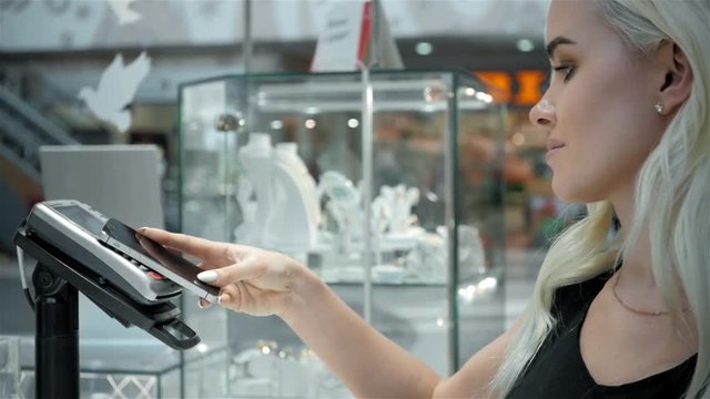 Woman blonde, fashion model shopping paying with NFC technology on mobile phone, in supermarket
