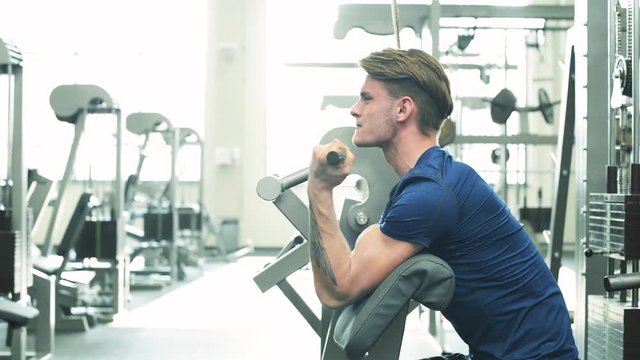Young man in gym working out, using weights machine for arms.