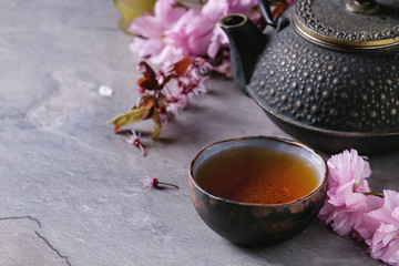 Black iron teapot and traditional ceramic cup of tea with blossom pink flowers cherry branch over...