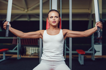 Beautiful girl doing exercises on the simulator in the gym dressed blank white tank-top and tights.