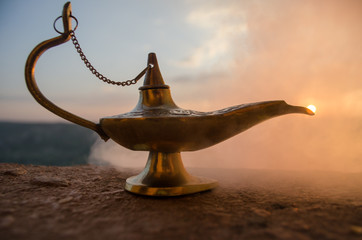 Antique artisanal Aladdin Arabian nights genie style oil lamp with soft light white smoke. Sunset...