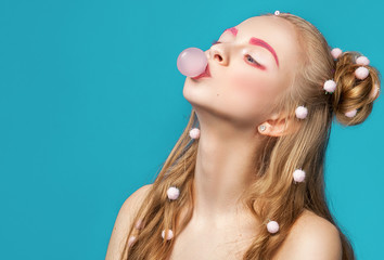 Young beautiful and funny woman blowing pink bubble gum over blue background.