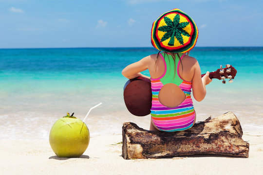 Little happy baby in rastaman hat have fun, play reggae music on Hawaiian guitar, enjoy relaxing on ocean beach. Children healthy lifestyle. Travel, family activity on tropical island summer holiday