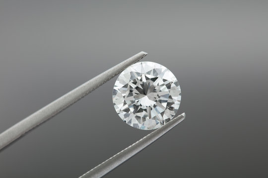 loose brilliant round diamonds is being held by tweezers on grey background