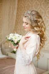 Pretty young girl. Blonde woman with luxurious long curly hair. Boudoir morning of the bride. Taking wedding bouquet in her hands