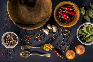 Food background with wooden bowls, vintage spoons, garlic, bay leaf, onion, turmeric, cumin, four kinds of spices, red pepper and black pepper.