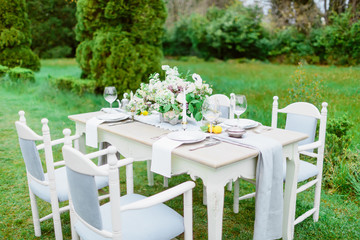 Table setting with dishes, cutlery, chairs and floristic in park. For wedding evening