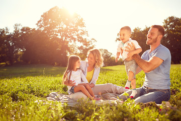 Young parents with children on picnic - obrazy, fototapety, plakaty