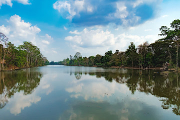 Obraz na płótnie Canvas Beautiful lake nestled among rainforest in Cambodia under blue sky with white clouds. It surrounding mysterious ruins of Angkor Thom in Siem Reap, Cambodia.