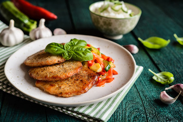 Fried pork fillets served with steamed zucchini, red bell pepper and garlic