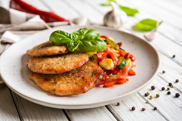 Fried pork fillets served with steamed zucchini, red bell pepper and garlic