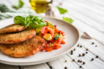 Fried pork fillets served with steamed zucchini, red bell pepper and garlic