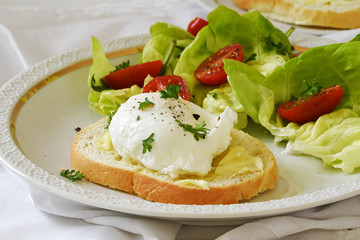 Fototapeta na wymiar Poached egg on baguette slice with salad and tomatoes on a white plate, delicious breakfast or snack