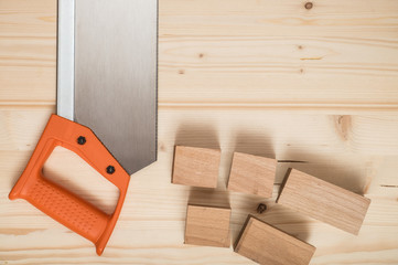 Hand saw with orange handle and sawn-off board on wooden background.