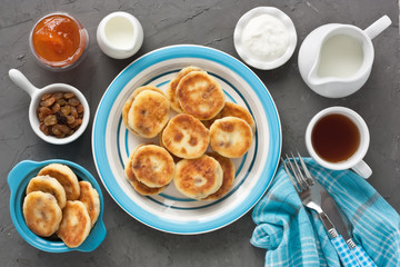 Cottage cheese pancakes / Cottage cheese pancakes with raisin, milk, sour cream, jam and cup tea for breakfast on dark stone rustic background
