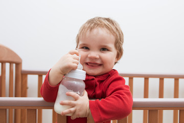 Adorable baby playing on a bed and drinking milk from a bottle