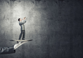 Young businessman on metal tray playing fife against concrete background