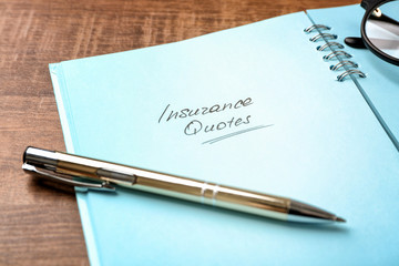 Text INSURANCE QUOTES written in notebook on wooden background