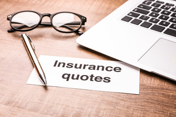 Card with text INSURANCE QUOTES, laptop and glasses on wooden background