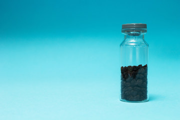 Black seeds in a glass vial on a blue background, space for text.