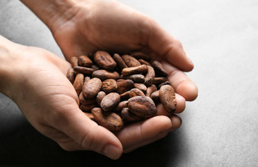 Female hands holding aromatic cocoa beans on gray background