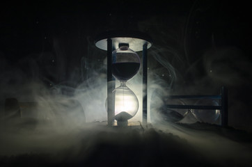 Time concept. Silhouette of Hourglass clock and smoke on dark background with hot yellow orange lighting, or symbols of time with copy space, sandglass or sand clock