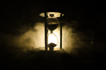 Time concept. Silhouette of Hourglass clock and smoke on dark background with hot yellow orange lighting, or symbols of time with copy space, sandglass or sand clock