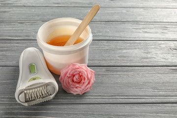 Modern epilator and plastic bucket with sugaring paste on wooden background