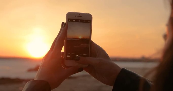 A girl is taking pictures of a sunset on a smartphone