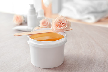 Plastic bucket with sugaring paste, wooden stick and flower on table