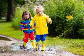 Fototapeta premium Kids play in rain and puddle in autumn